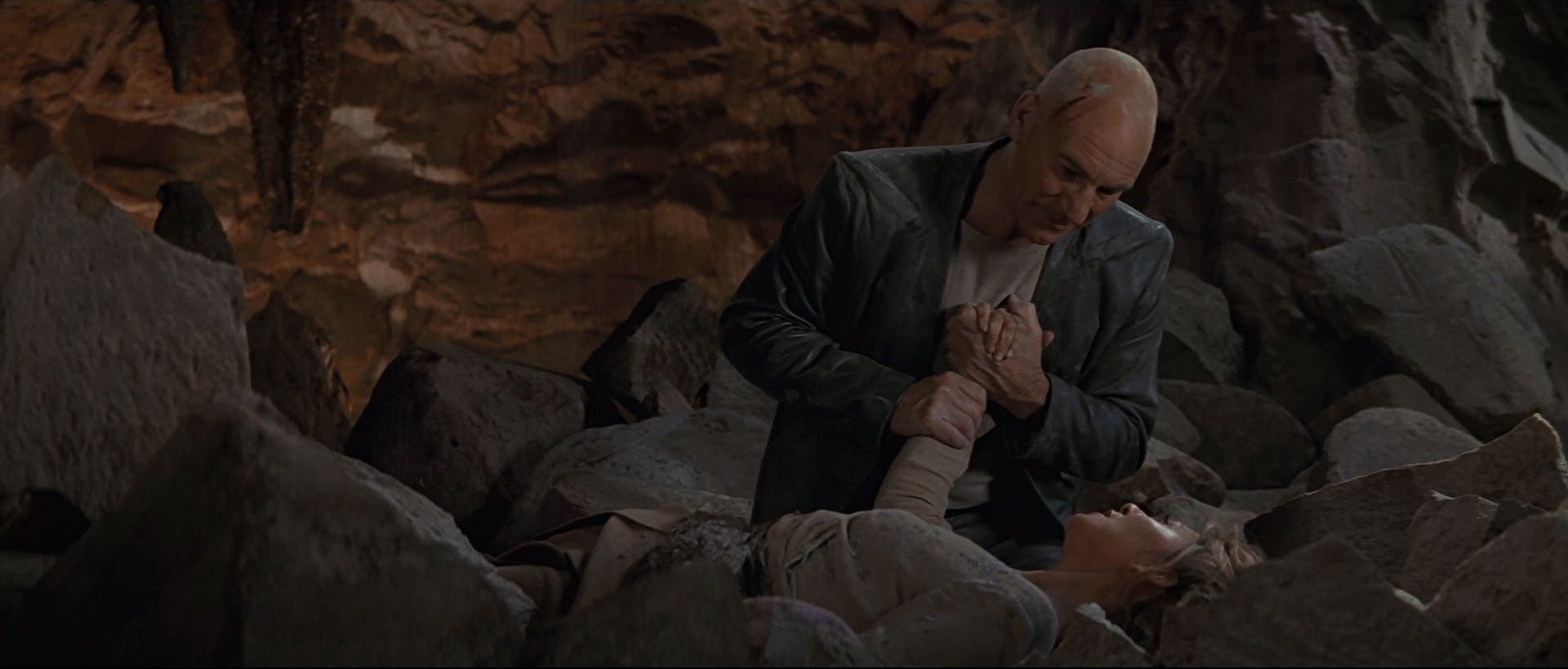 Struggling to keep Anij alive, as she's crushed under the cavern rubble, Picard holds her hand asking her to stay in the moment with him in Star Trek: Insurrection
