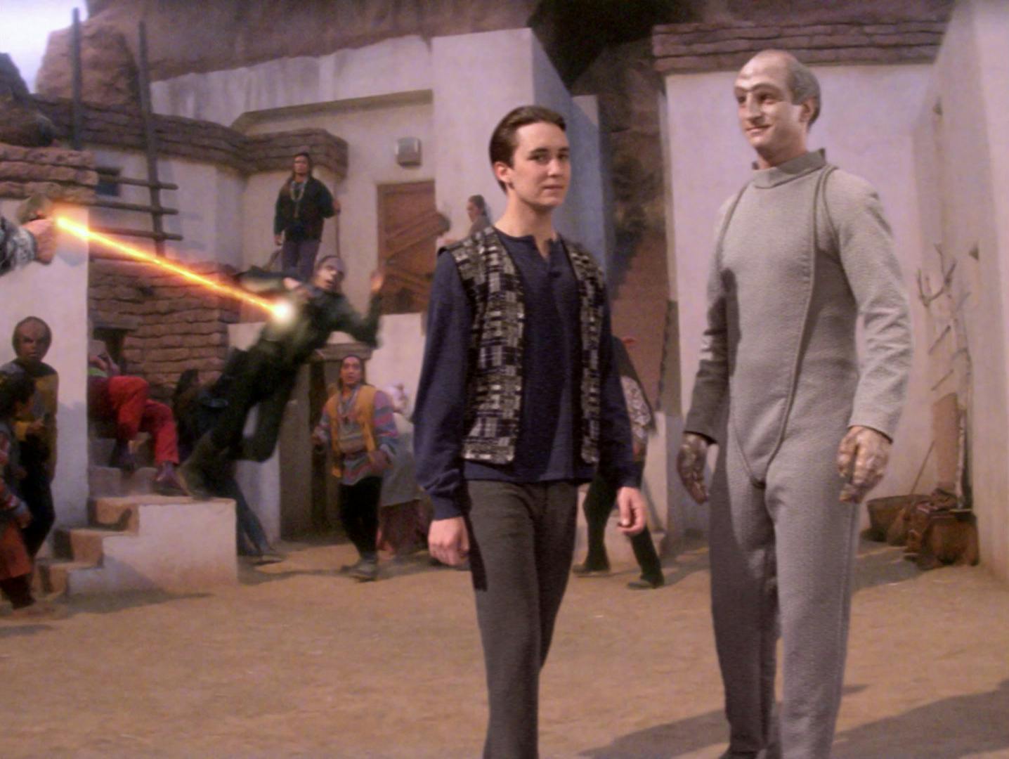 Wesley Crusher in local civilian attire walks away from a mele with the Cardassians with The Traveler in 'Journey's End'