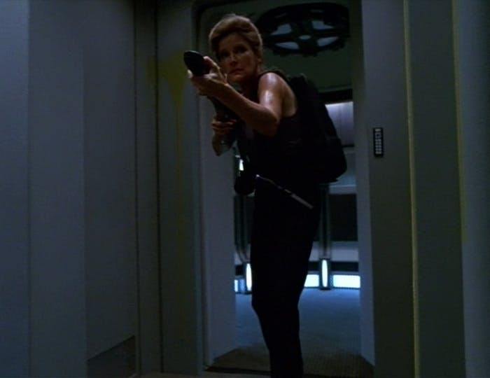 Captain Janeway in a tank and gear pack approaches a corridor while holding a phaser rifle in 'Macrocosm'