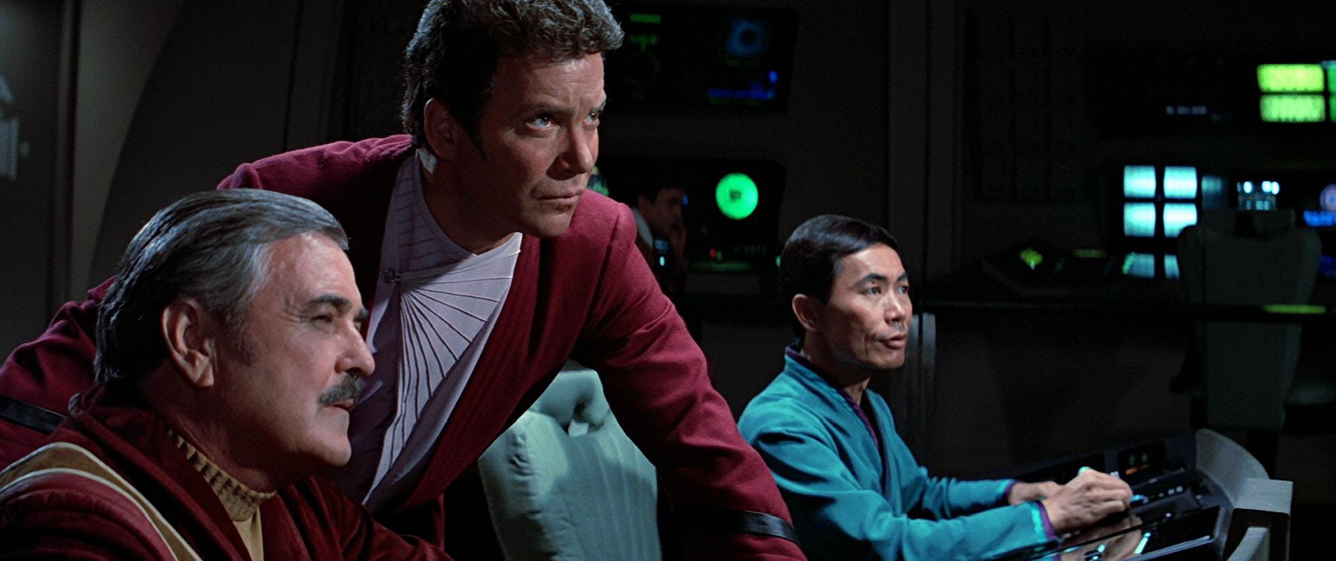 James Kirk leans over between Montgomery Scott and Hikaru Sulu at their stations as they all stare intently at the viewscreen in front of them in Star Trek: The Search for Spock