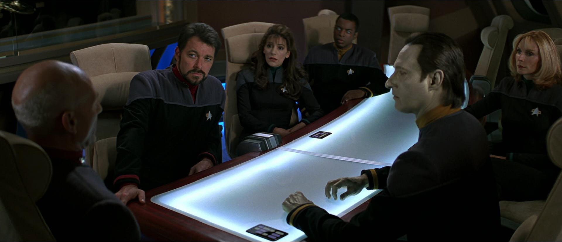 The Enterprise crew Riker, Deanna Troi, La Forge, Data, and Beverly Crusher gather at the Enterprise Observation Lounge with Jean-Luc Picard at the head of the table in Star Trek: First Contact
