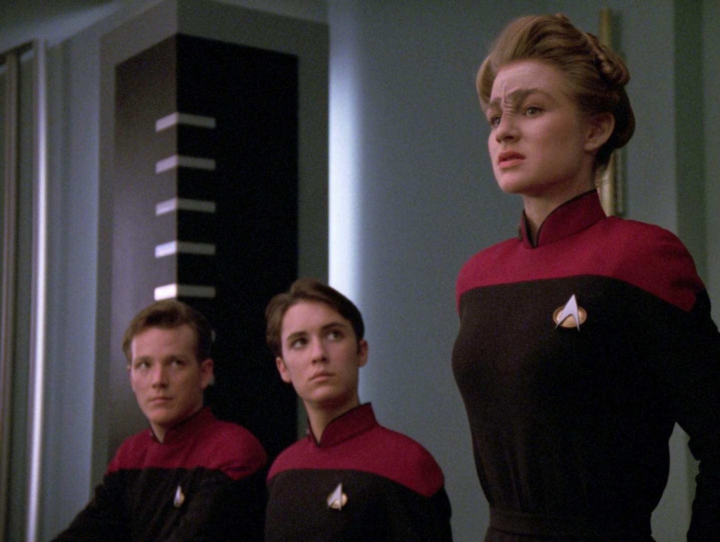 At their hearing, Sito Jaxa stands and answers a line of questioning as Nick Locarno and Wesley Crusher are seated, and looking up, next to her in 'The First Duty'