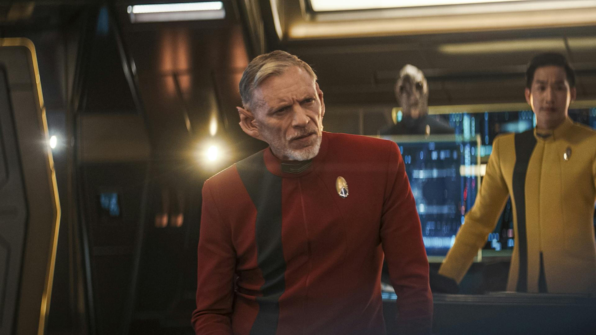 Rayner narrows his gaze towards the viewscreen ahead of him on the bridge of Discovery as Rhys and Linus stand behind him at their stations in 'Mirrors'