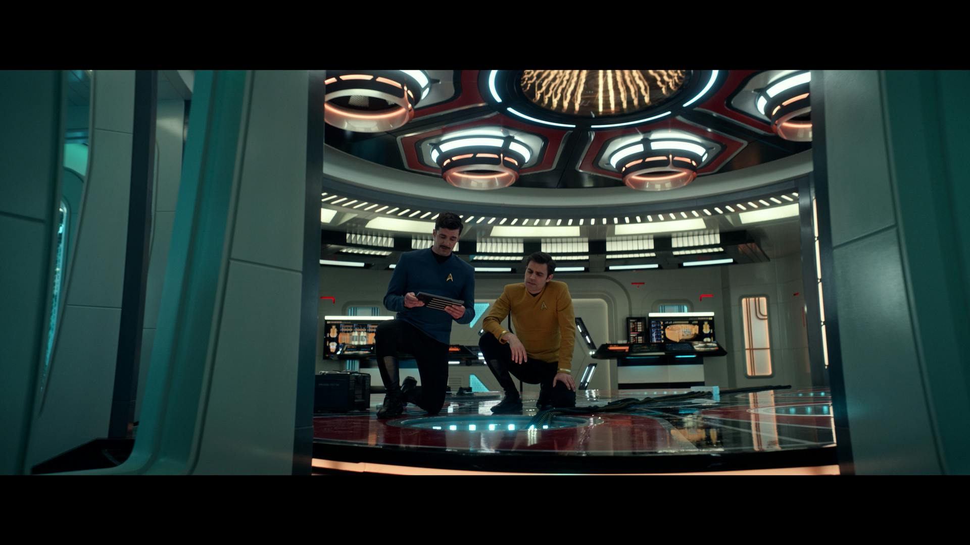 Sam and James Kirk both kneel in the Transporter Room on a transporter pad as they access it in 'Subspace Rhapsody'