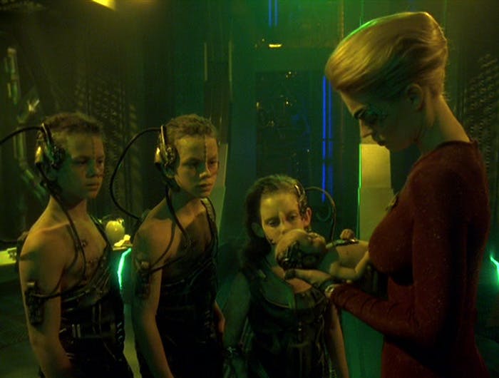 Aboard a Borg cube, Seven of Nine holds a Borg infant as three young Borg drones look over in 'Collective'