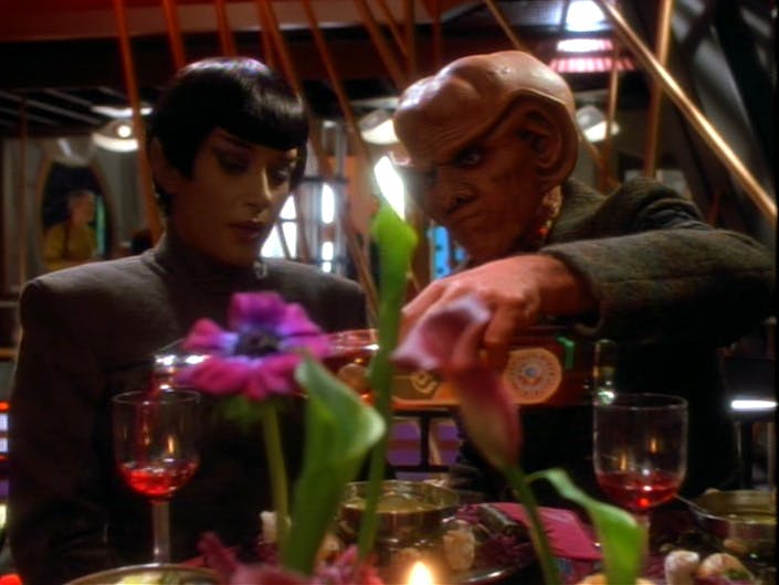 Arranging a business dinner, Quark pours a drink for the Vulcan Sakonna in 'The Maquis, Part I'
