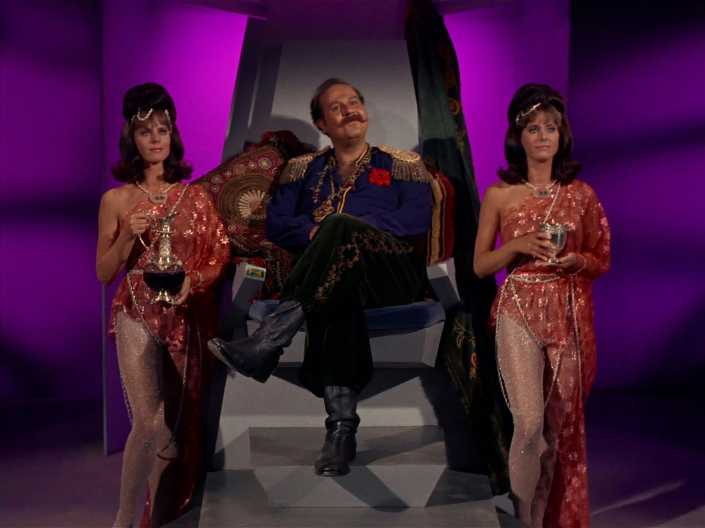 Harry Mudd sits on a throne as ruler of an android planet and flanked by two women servants by his side in 'I, Mudd'