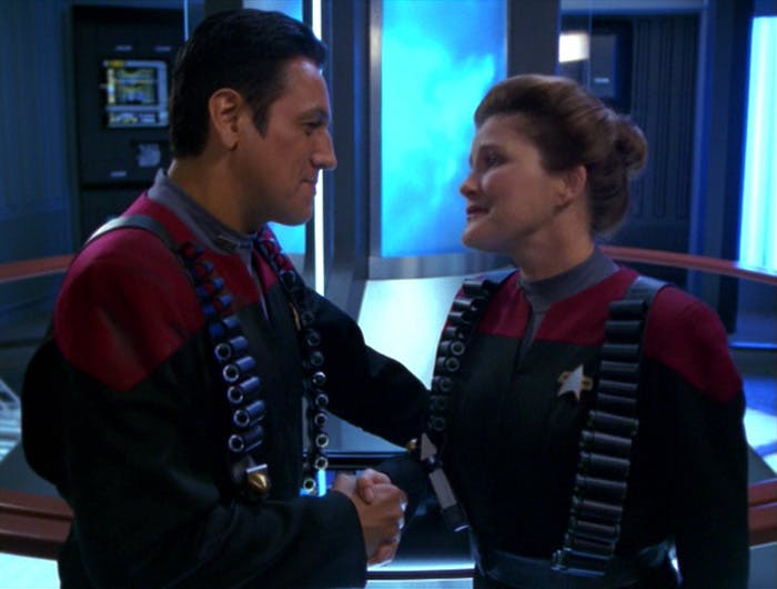 Chakotay and Janeway with tactical supplies strapped to their bodies look into each other's faces as they shake hands in 'Shattered'
