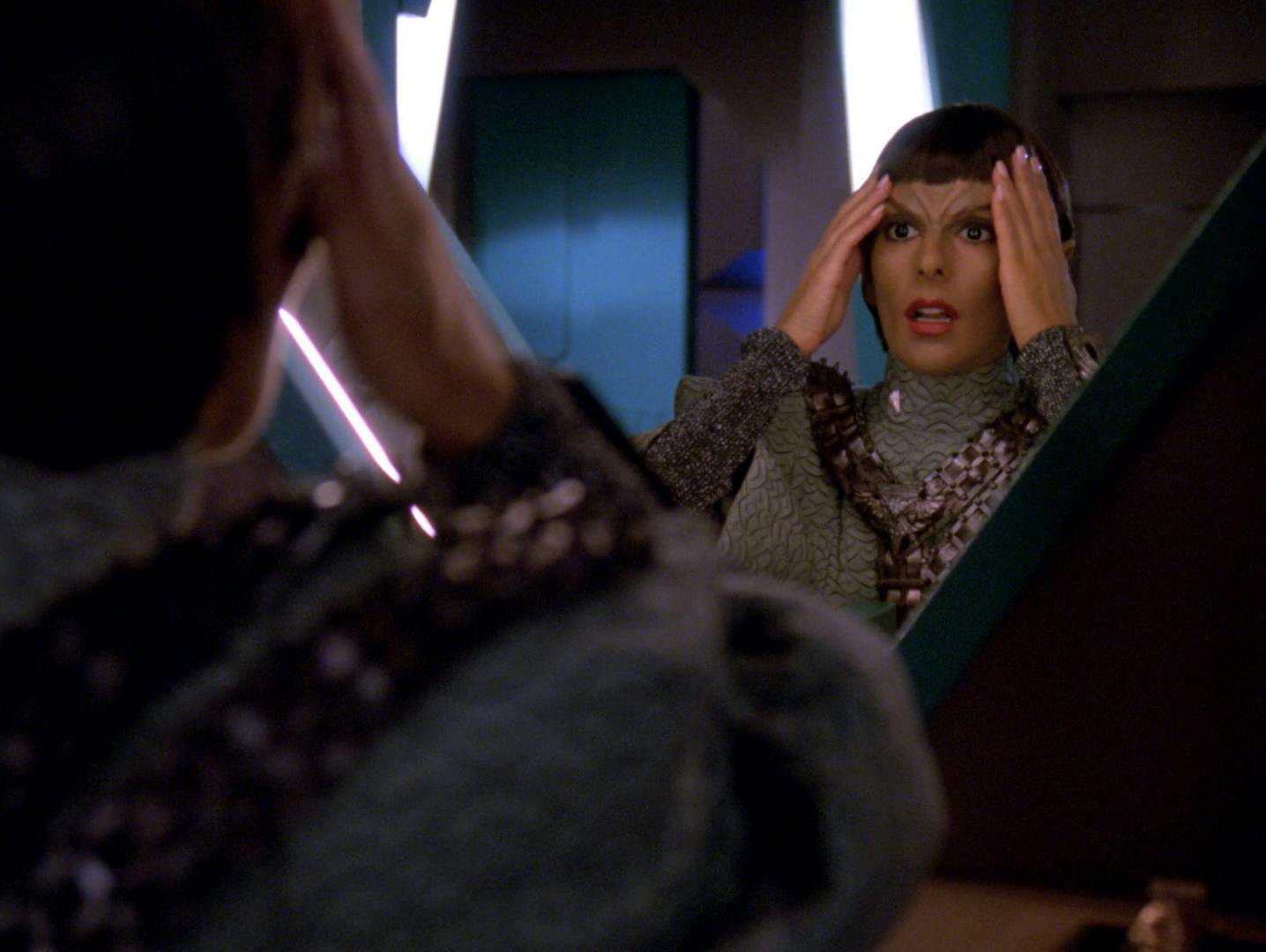 Deanna Troi expresses shock and horror as she raises her hands to her face upon discovering she has been altered to appear as a Romulan in 'Face of the Enemy'