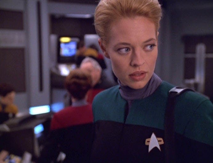 Seven of Nine stands on the bridge of Voyager. Her Borg implants are gone, and she is wearing a Starfleet uniform in 'Relativity'