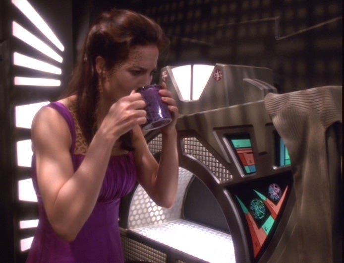 A disheveled Jadzia Dax grips and drinks from her raktajino mug in 'You Are Cordially Invited...'