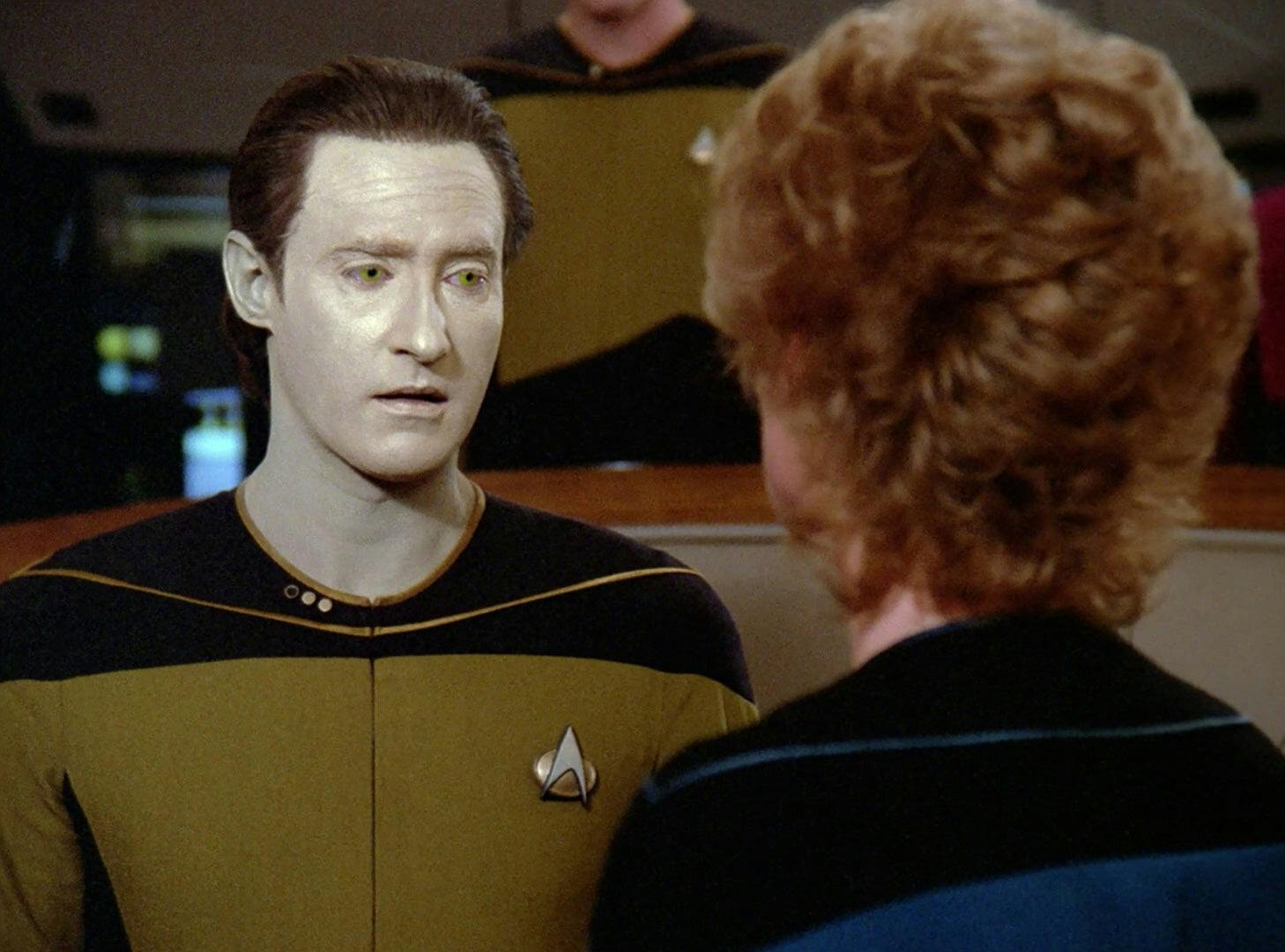 Dr. Pulaski stands in front of Data who looks slight to the right of her on the bridge of the Enterprise in 'Peak Performance'