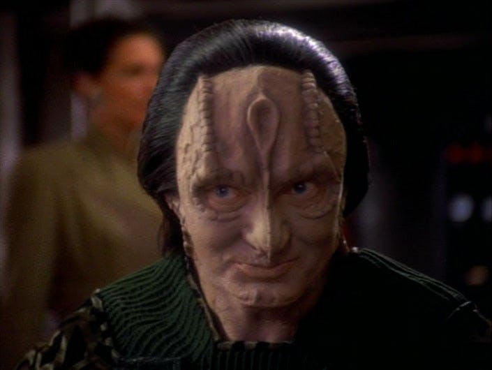 Garak smiles while chatting with Bashir in the replimat