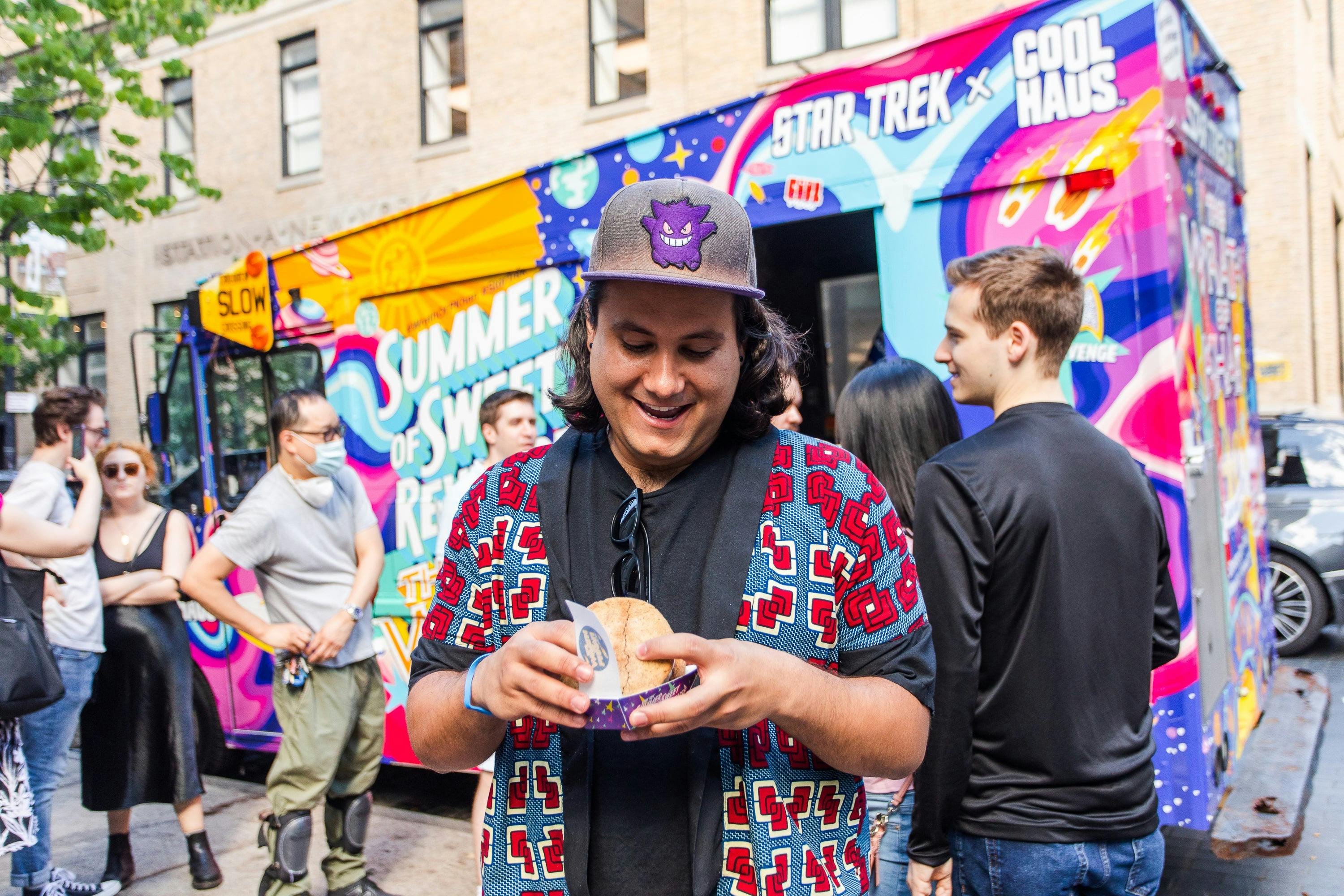 A man in a baseball hat looks excitedly at his ice cream sandwich.