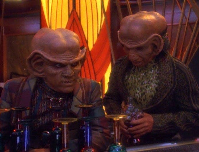Quark and Rom flanked by various glasses at the bar counter in 'The House of Quark'