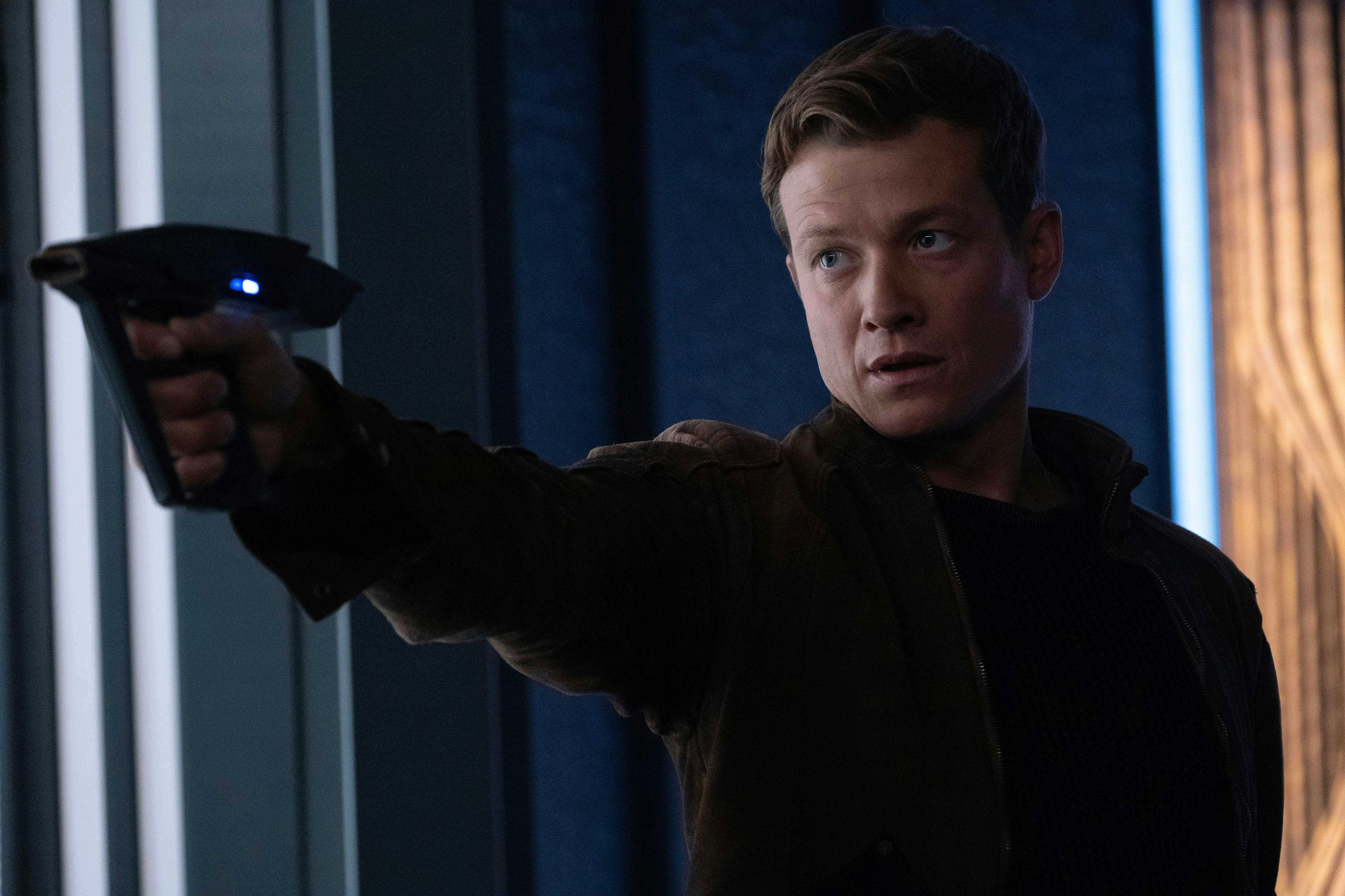 Ed Speleers as Jack stands defensive with his phaser pointed in front of him on Star Trek: Picard