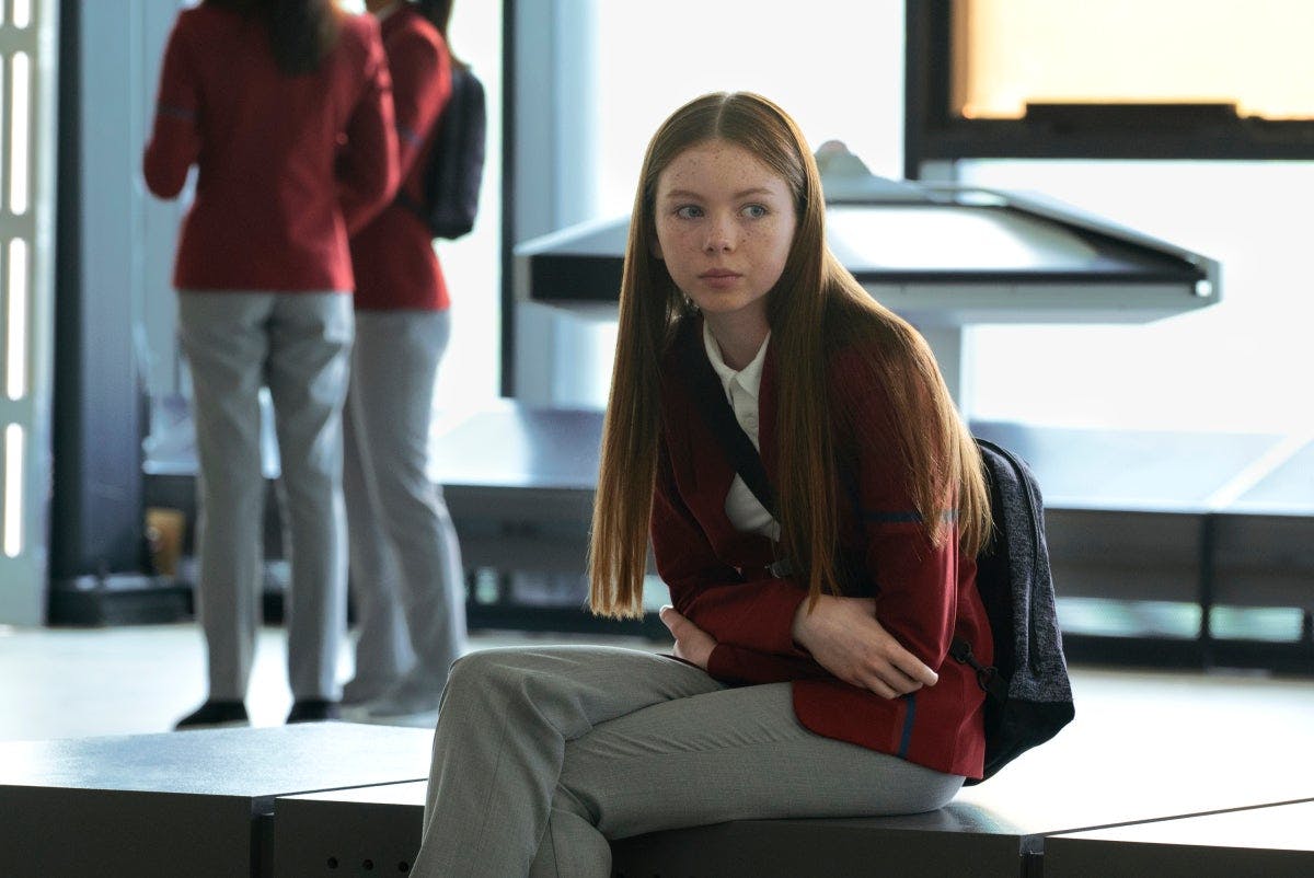 Lil in her school uniform and with her backpack on sits in the school's common area in 'Children of Mars'