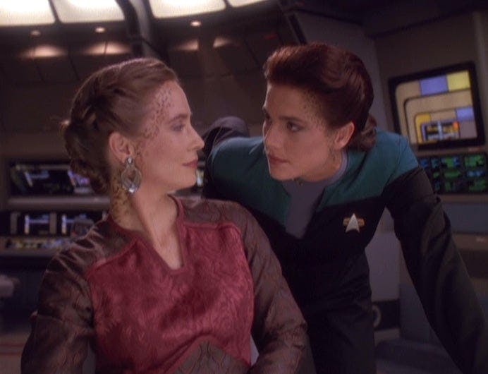 A seated Lenara Kahn looks over her shoulder and Jadzia Dax crouches over her in 'Rejoined'