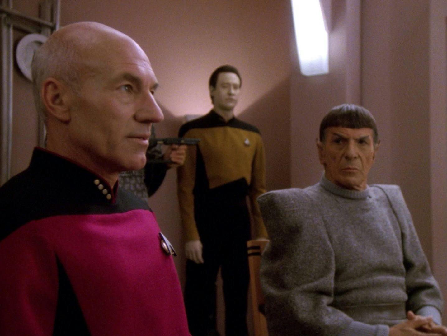 Captain Picard and Spock are held at phaser point. Data stands nearby.