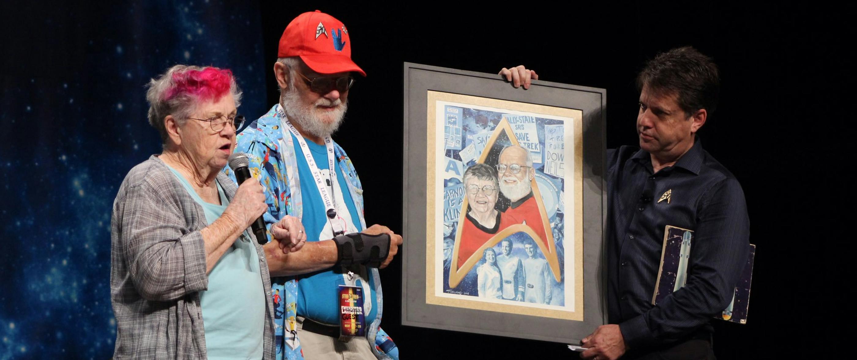 For the 50th anniversary celebration at Star Trek Last Vegas, John Van Citters invites Bjo and John Trimble to recognize their efforts and present them with a painted portrait from artist JK Woodward