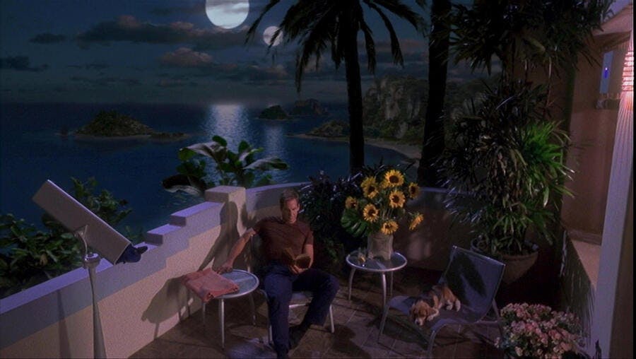 Archer enjoying a book and Porthos' company on the patio of his Risean villa by moonlight in 'Two Days and Two Nights'