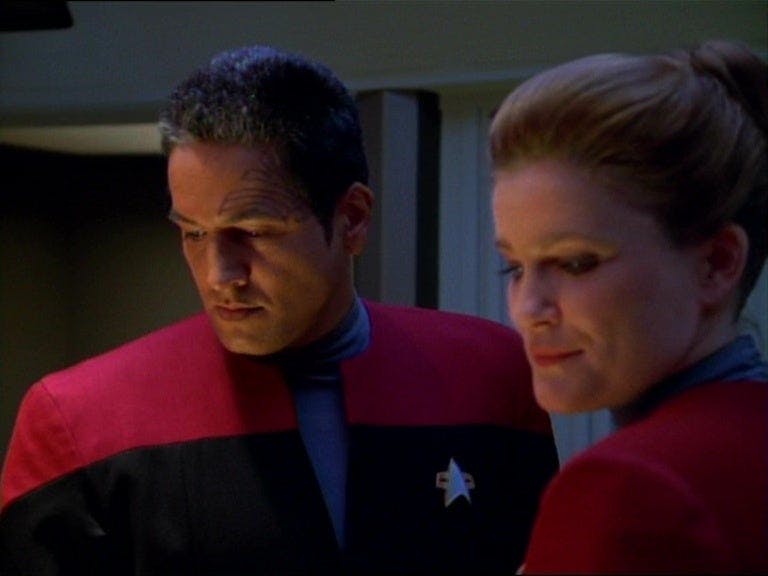 Chakotay and Janeway stand next to each other, looking at a screen, in 'Parallax'