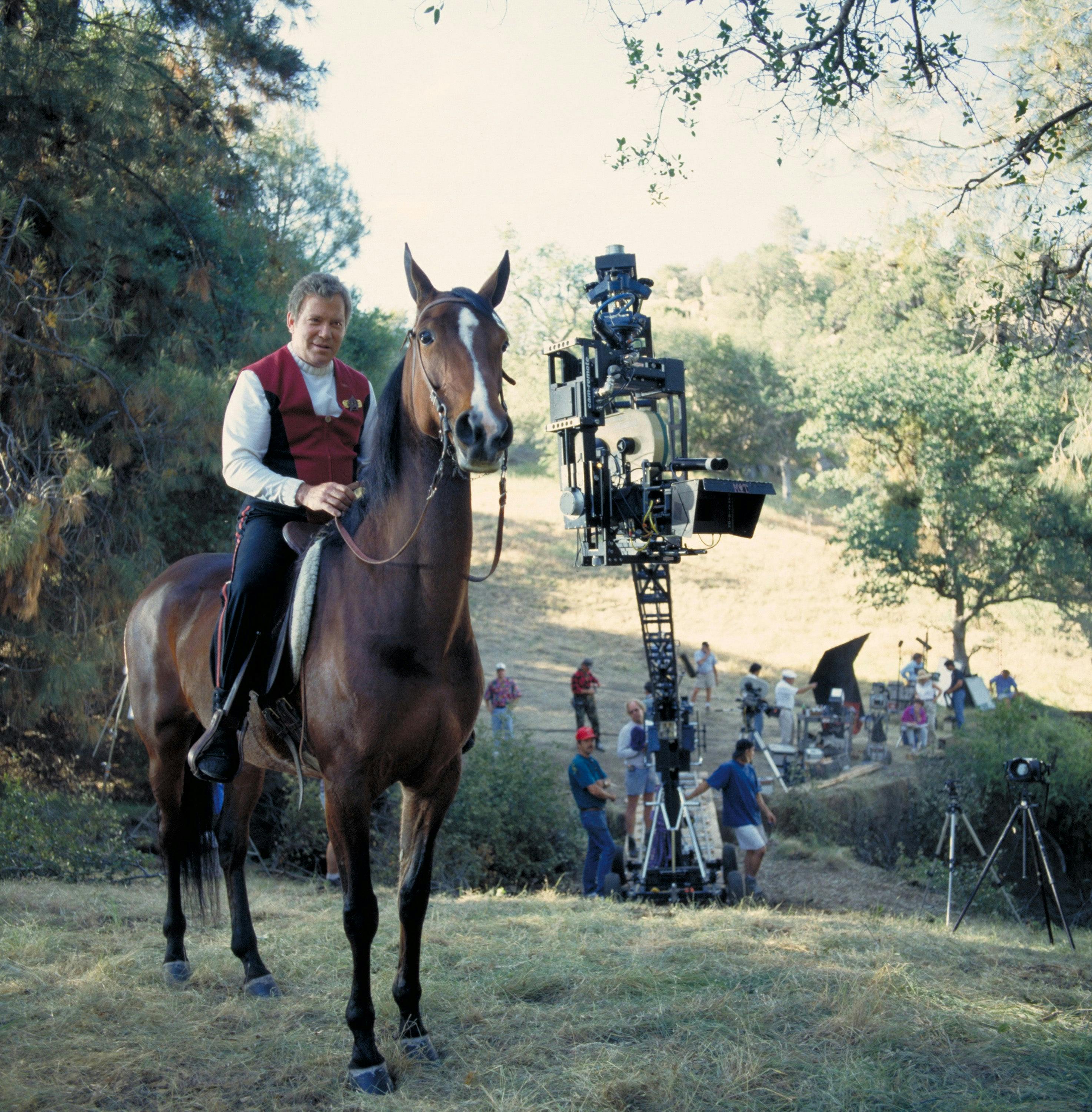 William Shatner on a horse (left) with camera and crew behind them, on set of Generations