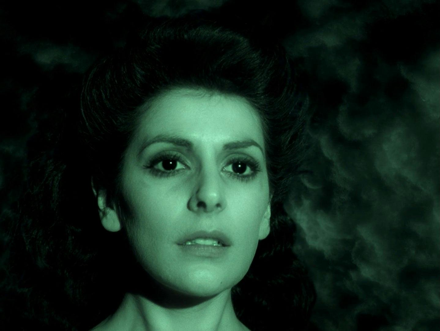 A close up of Deanna Troi bathed in green light.