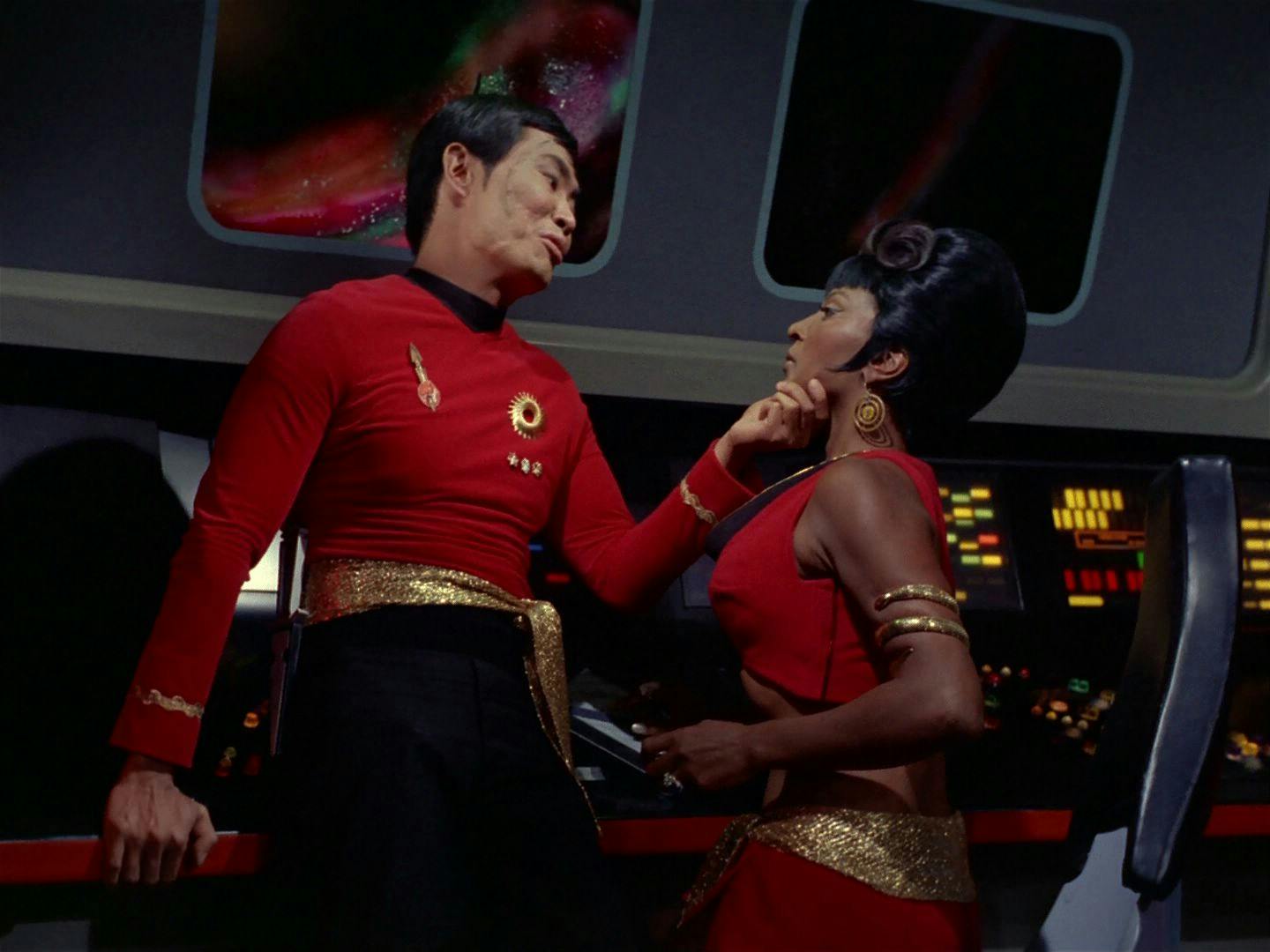 Mirror Sulu takes Mirror Uhura's face into his hand as he leans against her console