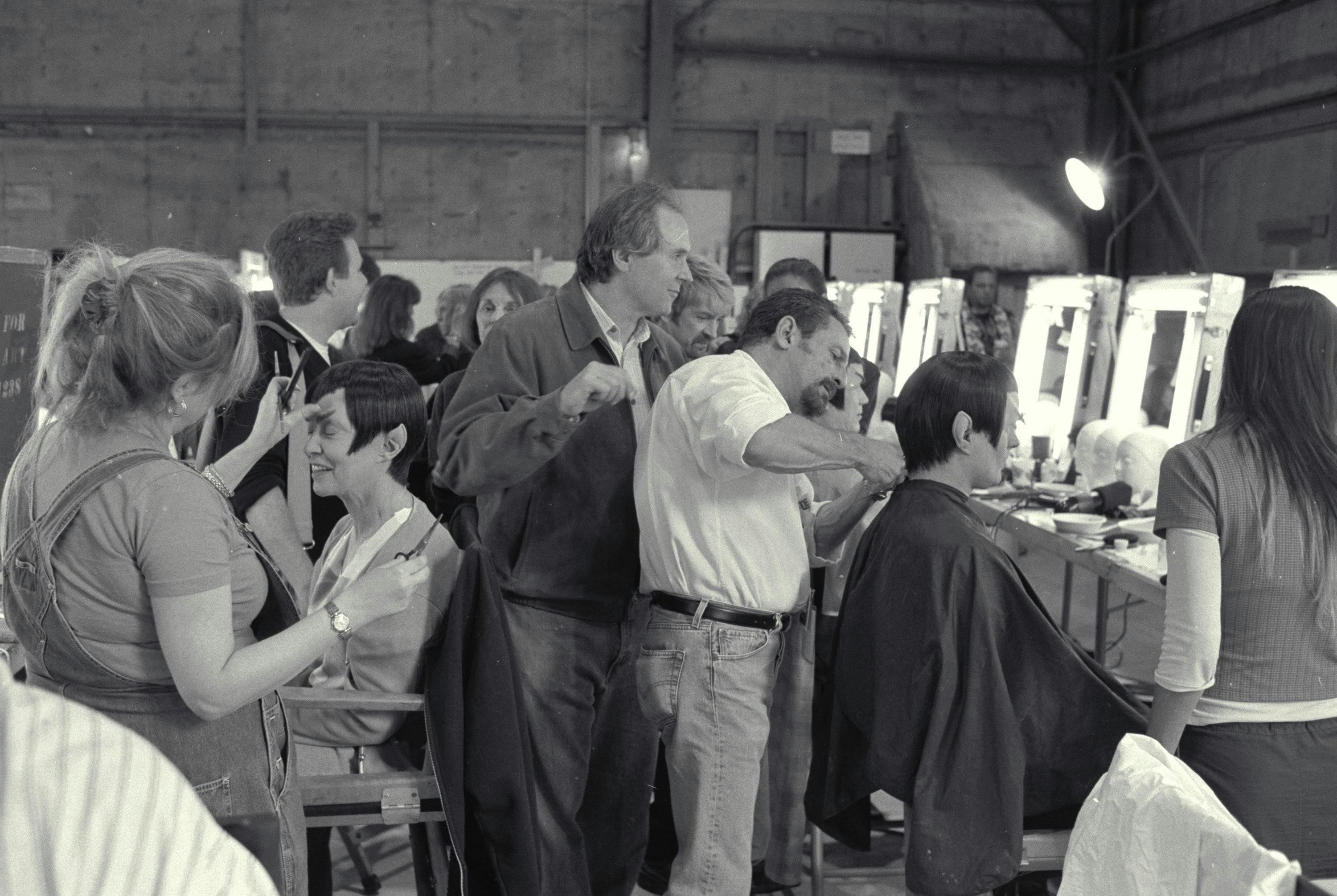 Black and white photo of numerous make-up mirrors and chairs on set of Star Trek Nemesis, featuring a variety of actors getting final touches on their Vulcan make-up.
