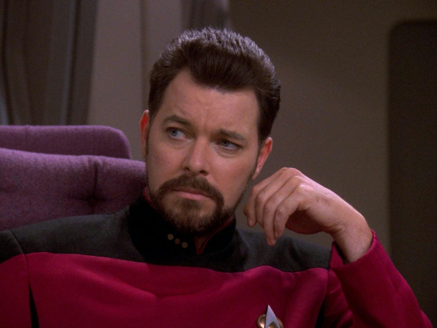 A glum Will Riker looks over and raises his hand to his face to rest on in 'Second Chances'
