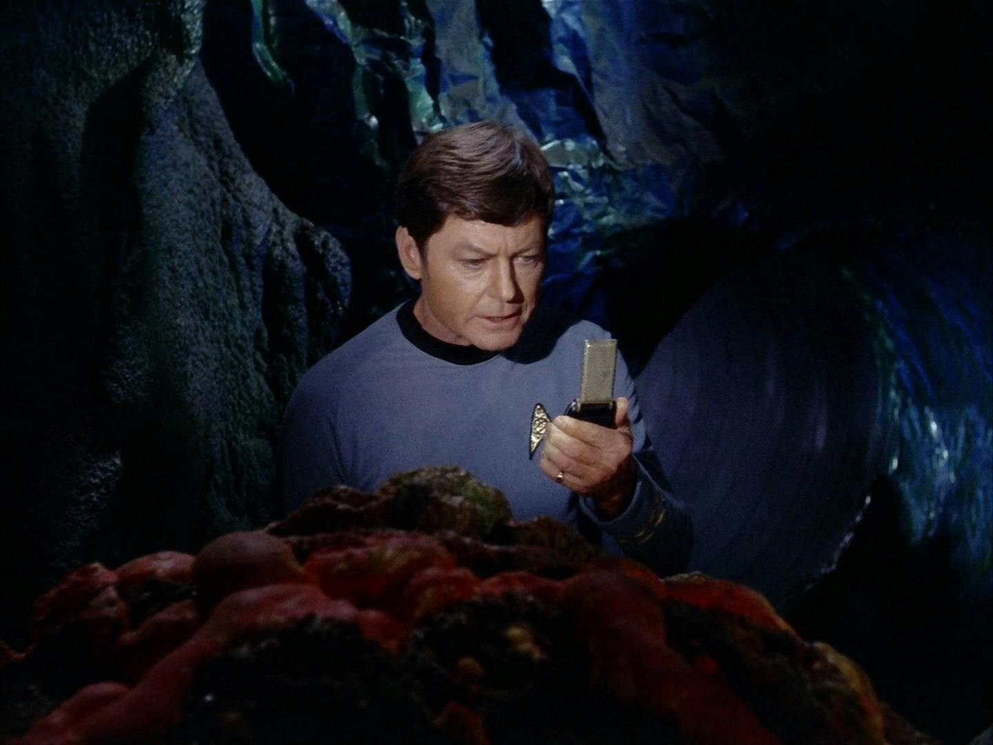 In a cave, McCoy examines the rocky-skinned alien as he lifts his communicator up in 'The Devil in the Dark'