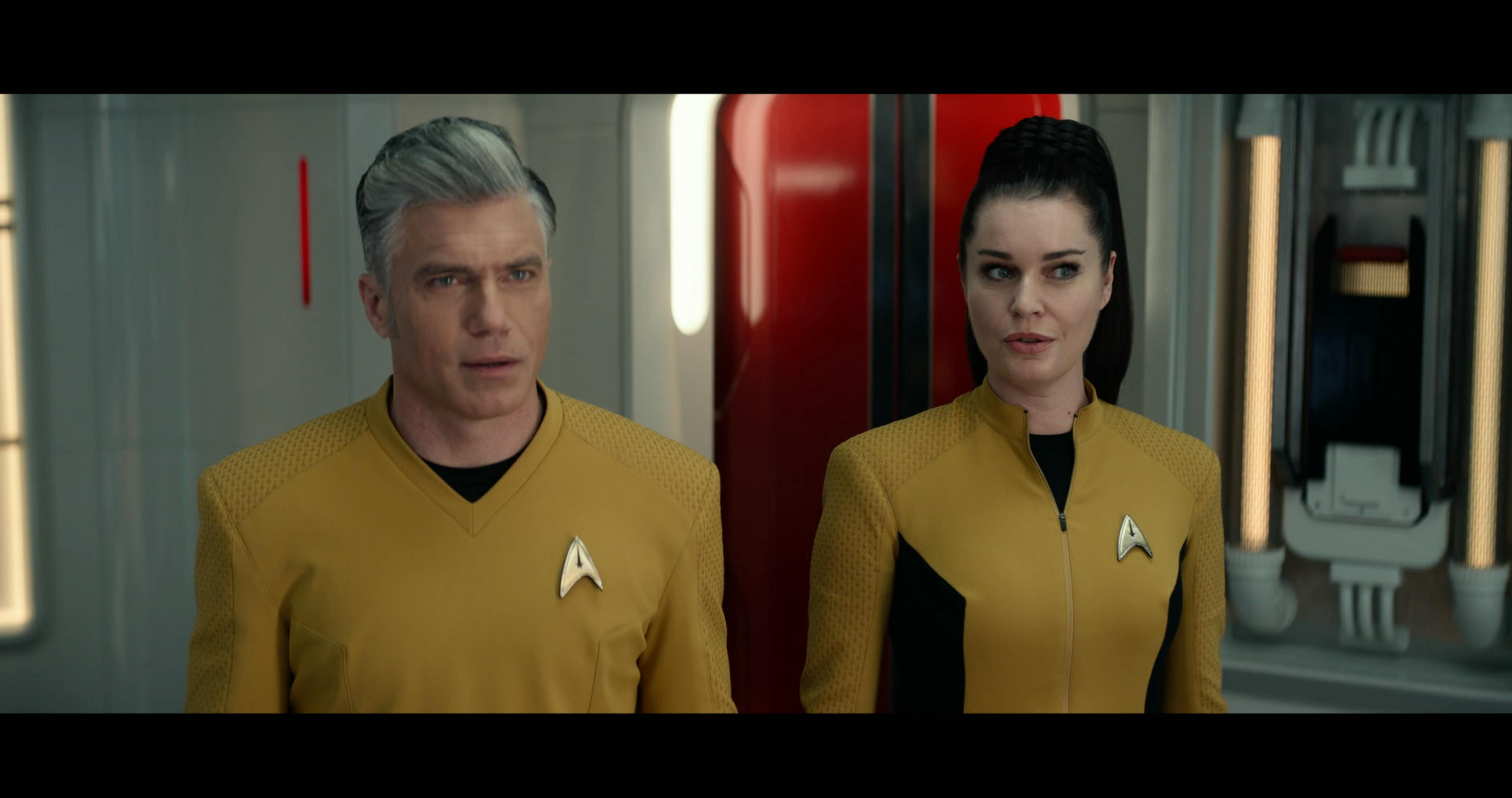 Captain Pike and Number One (Strange New Worlds) stand in the transporter room. Pike looks shocked, and Number One looks slightly confused as well.