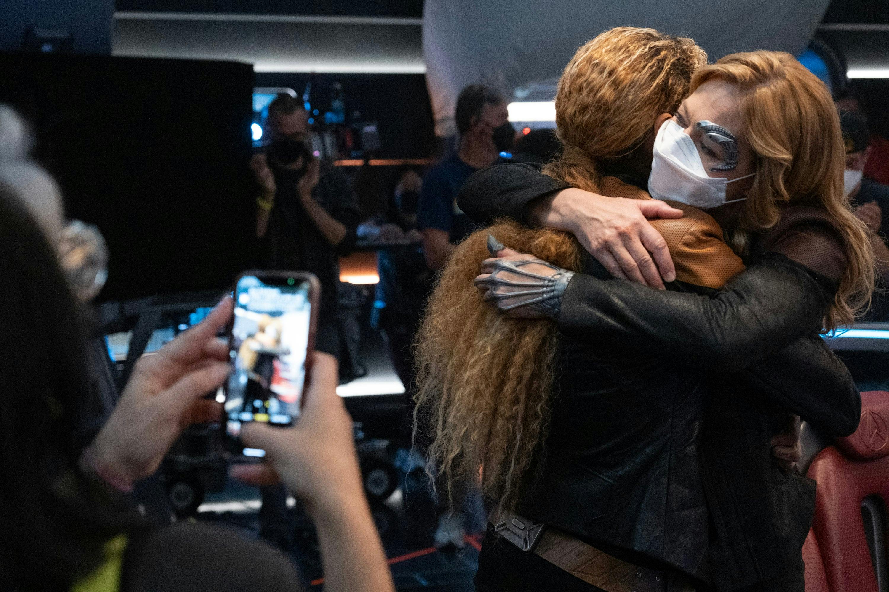 Star Trek: Picard BTS still - Michelle Hurd and Jeri Ryan hug as a production member takes a photo