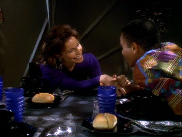 Over the meal table, Jake Sisko and his girlfriend Mardah huddle close gazing into each other eyes and clasping hands in 'The Abandoned'