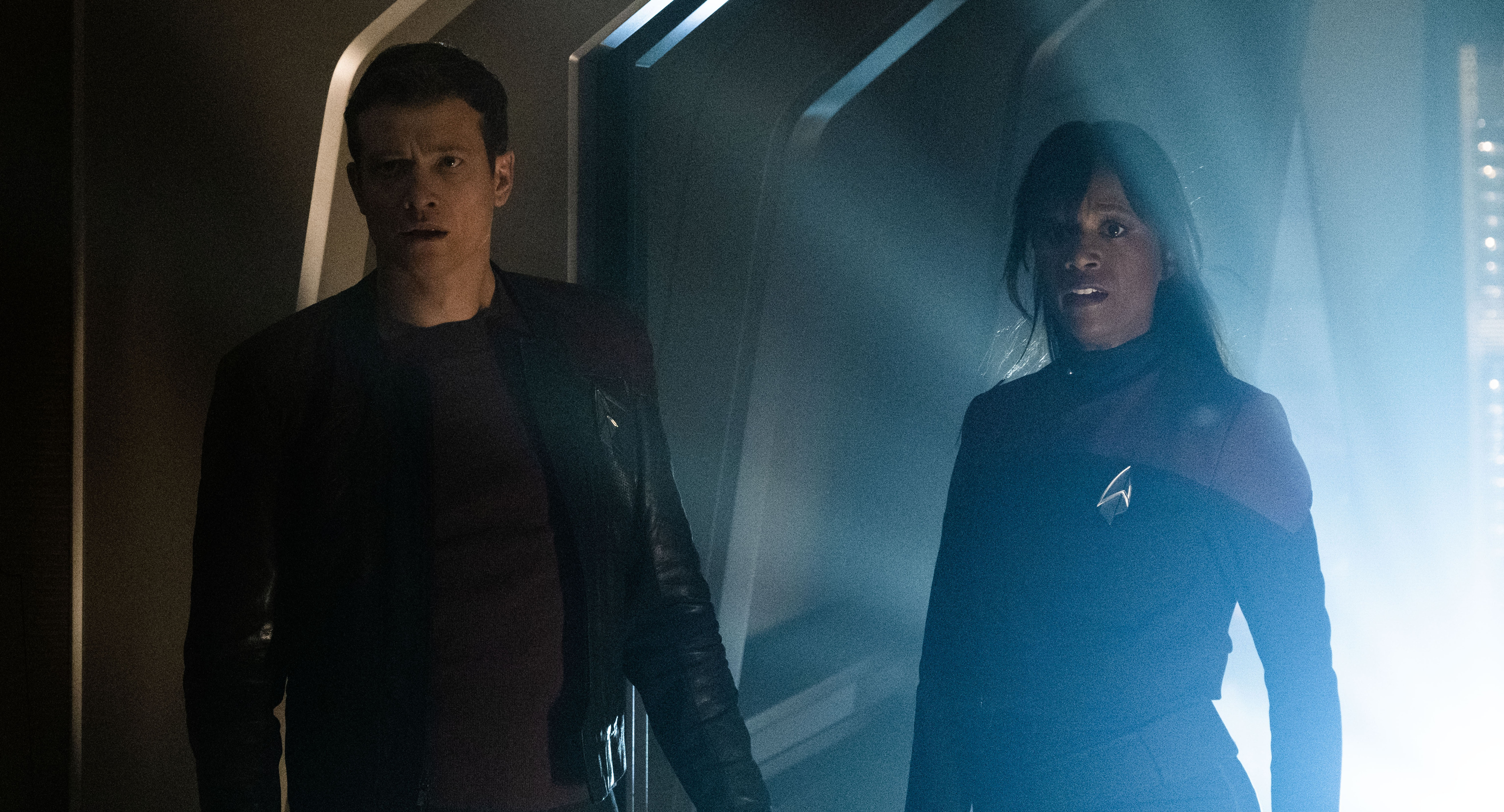 Jack Crusher and Sidney La Forge stand in the shadows and look ahead of them