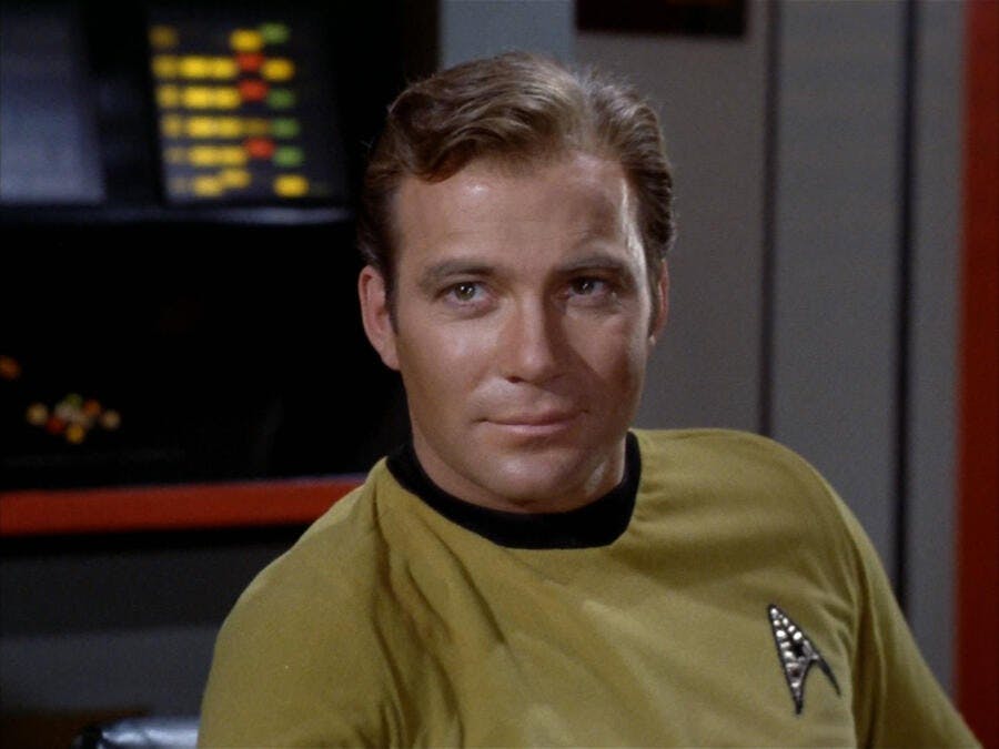 Captain Kirk (The Original Series) sits in the captain's chair, smiling slightly.
