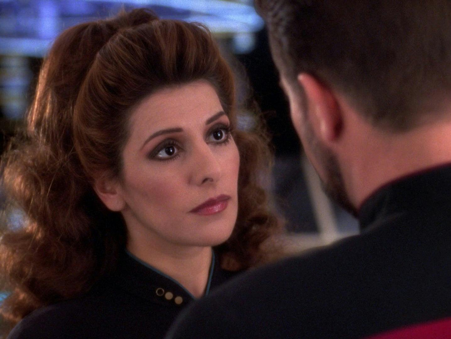 Counselor Deanna Troi looks up at Riker with a stoic expression on her face in 'Thine Own Self'
