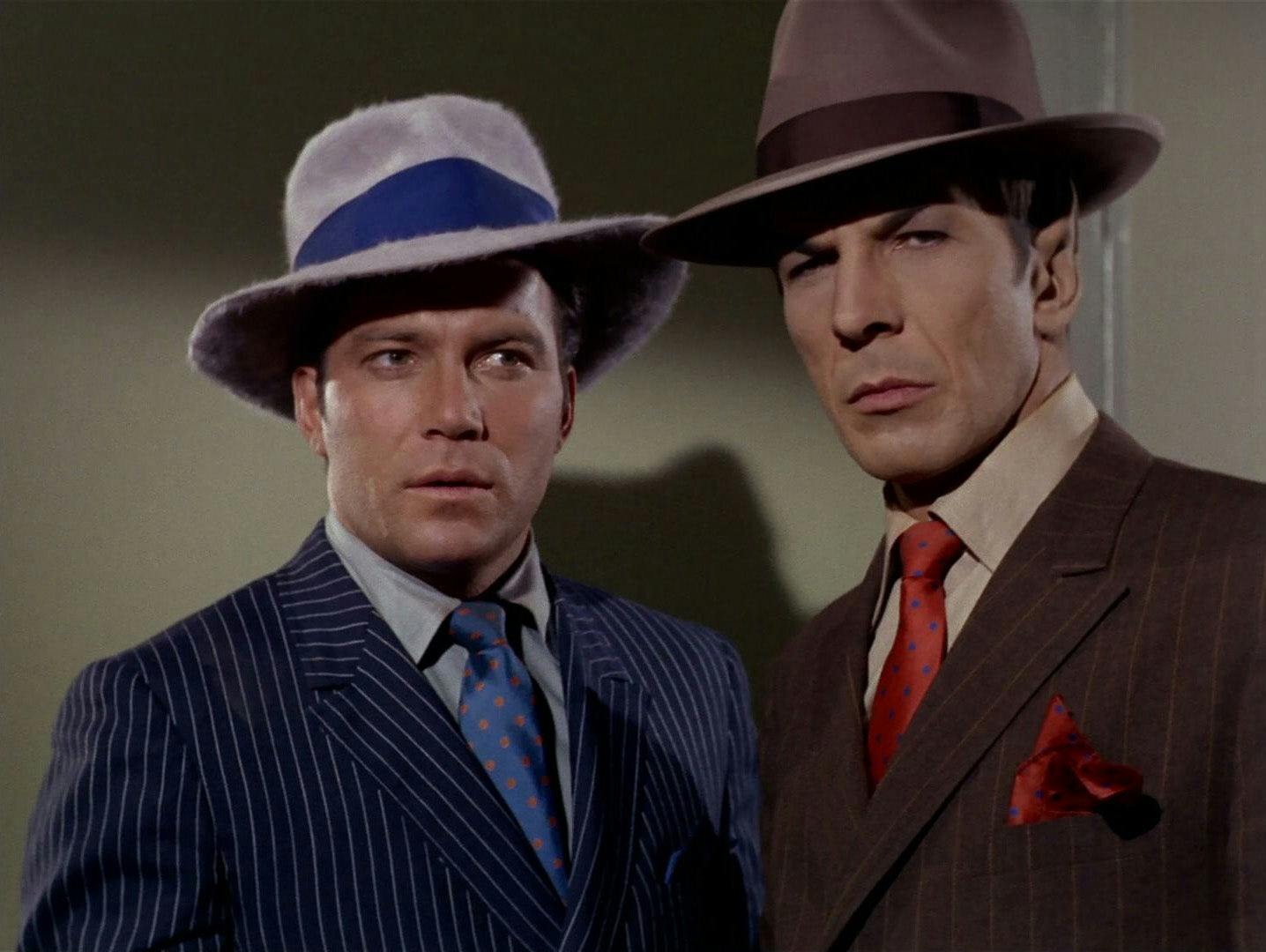 Kirk and Spock assess the situation while wearing 1920s mobster clothes and fedoras.