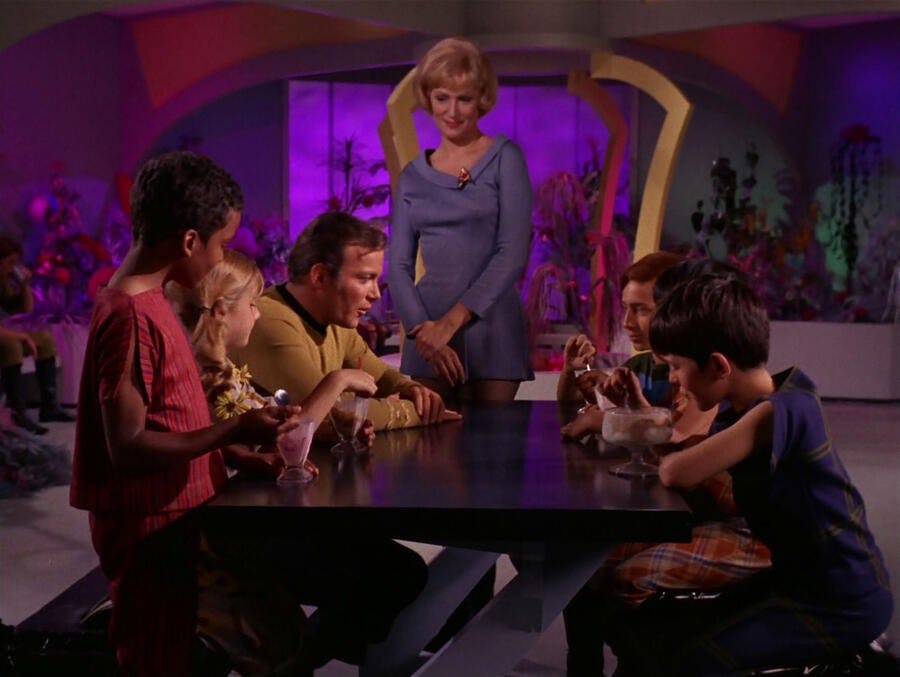 Kirk surrounded by a table full of kids enjoying ice cream in 'And The Children Shall Lead'