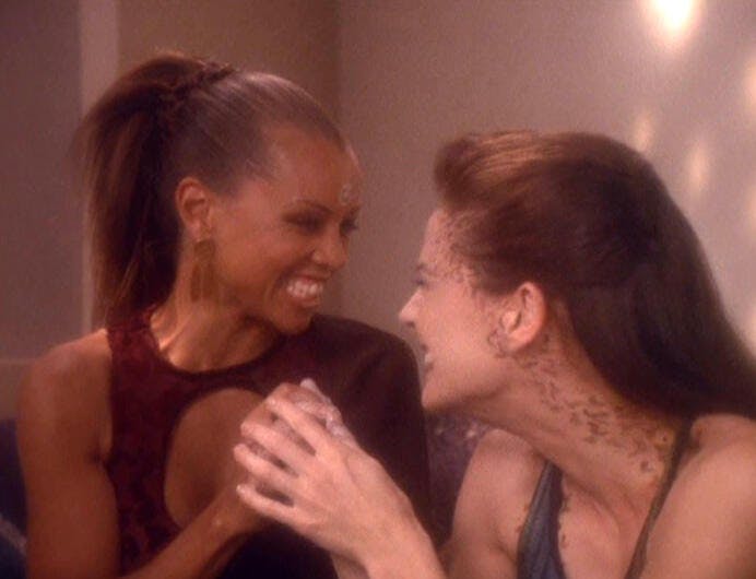 Arandis and Jadzia Dax intimately grin at each other while holding hands in 'Let He Who is Without Sin...'