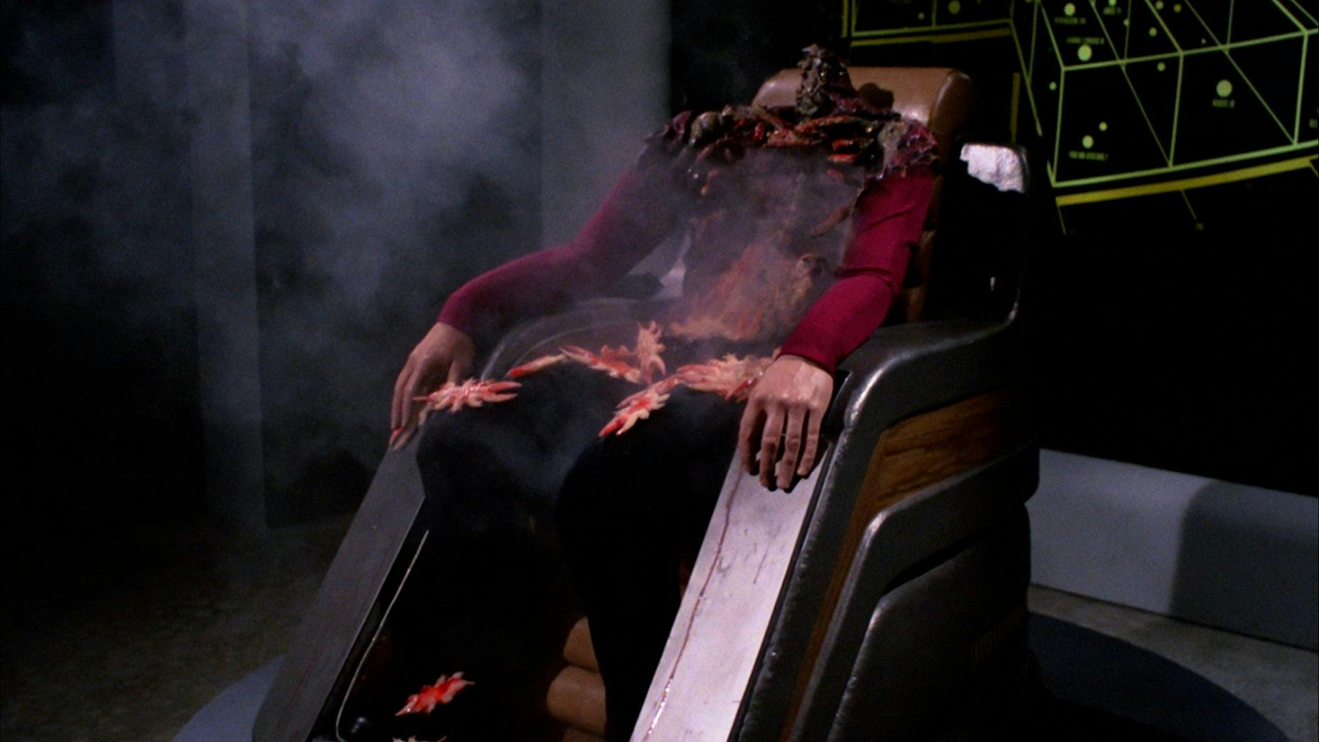 A headless Starfleet captain sits in a chair, with their skeleton partially exposed.