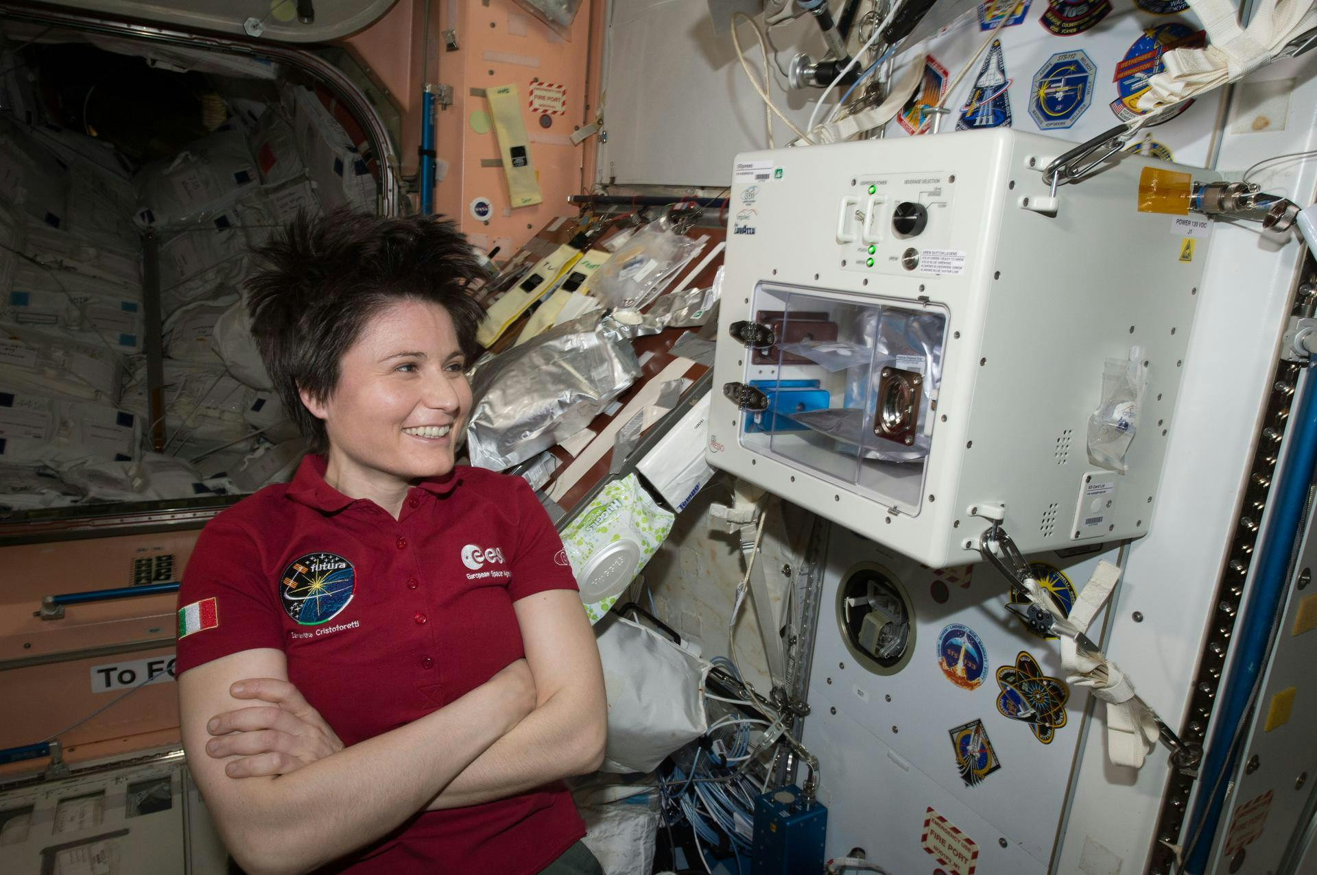 ESA (European Space Agency) astronaut Samantha Cristoforetti waits next to the newly installed ISSpresso machine. The espresso device allows crews to make tea, coffee, broth, or other hot beverages they might enjoy.