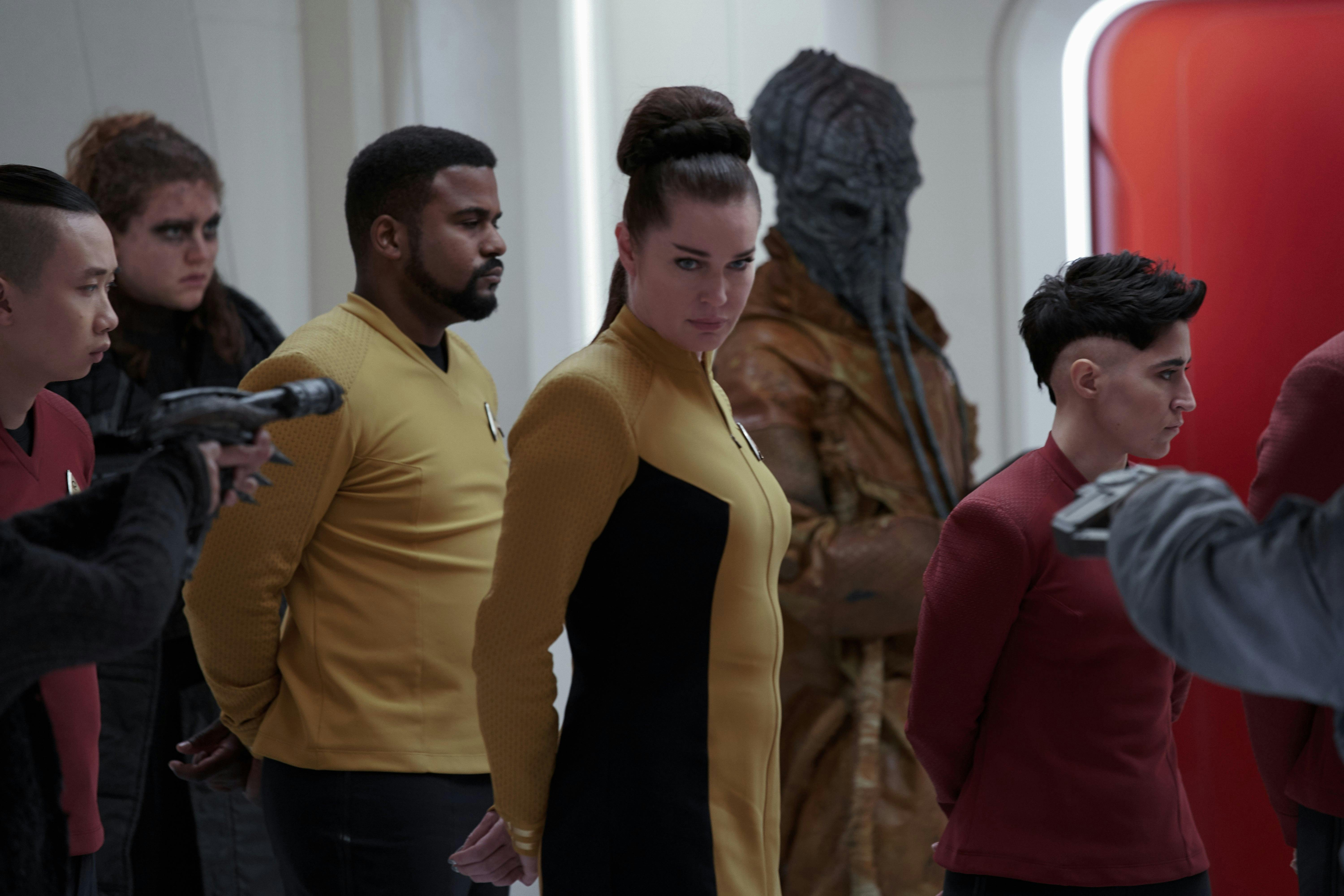 Number One (Rebecca Romijn) is in medbay, along with several other crewmembers including Erica Ortegas (Melissa Navia). Her hands are cuffed behind her back and she is looking to the side.