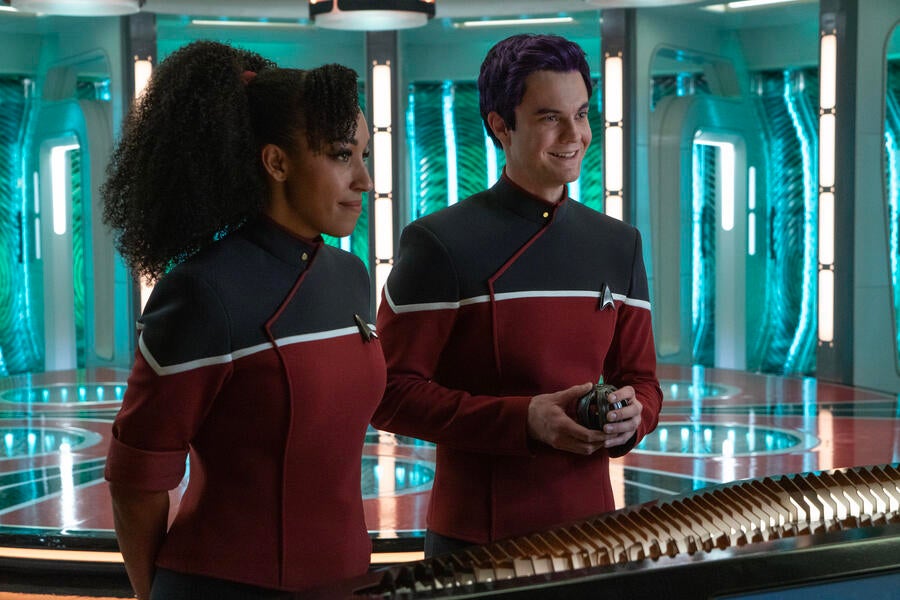 The live action versions of Beckett Mariner and Brad Boimler in their Cerritos Starfleet uniform in front of the Enterprise&#x27;s transporter pad