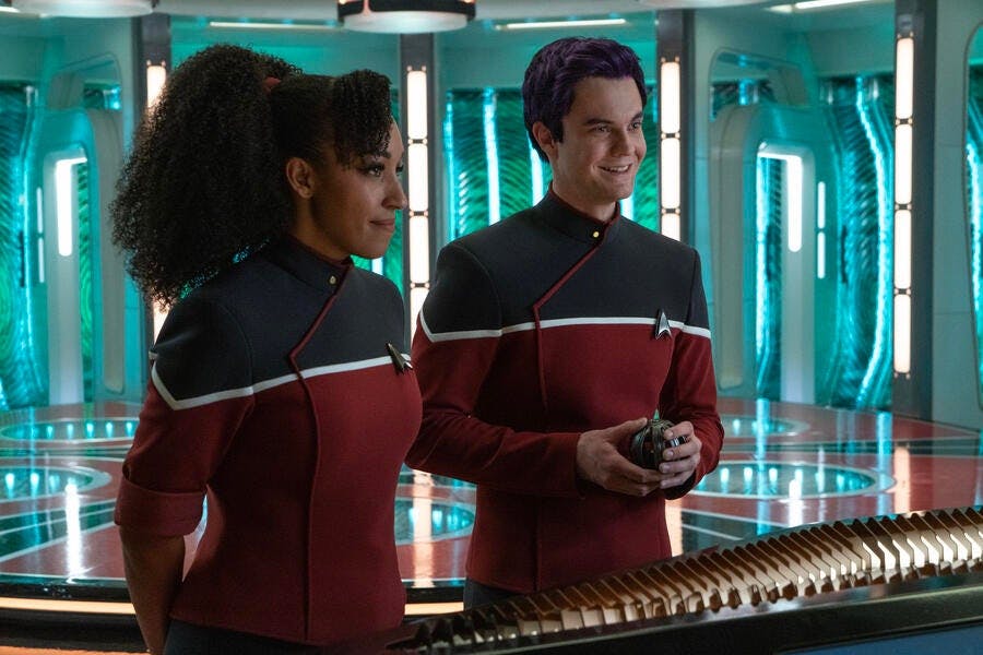 The live action versions of Beckett Mariner and Brad Boimler in their Cerritos Starfleet uniform in front of the Enterprise's transporter pad