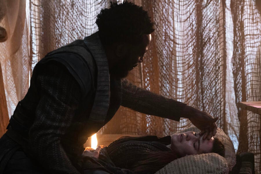 M'Benga raises his hand to feel a wounded and feverish La'An's temperature as she lays down on a cot in 'Among the Lotus Eaters'