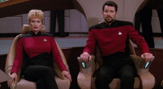 Riker sits in the captains chair on the bridge.
