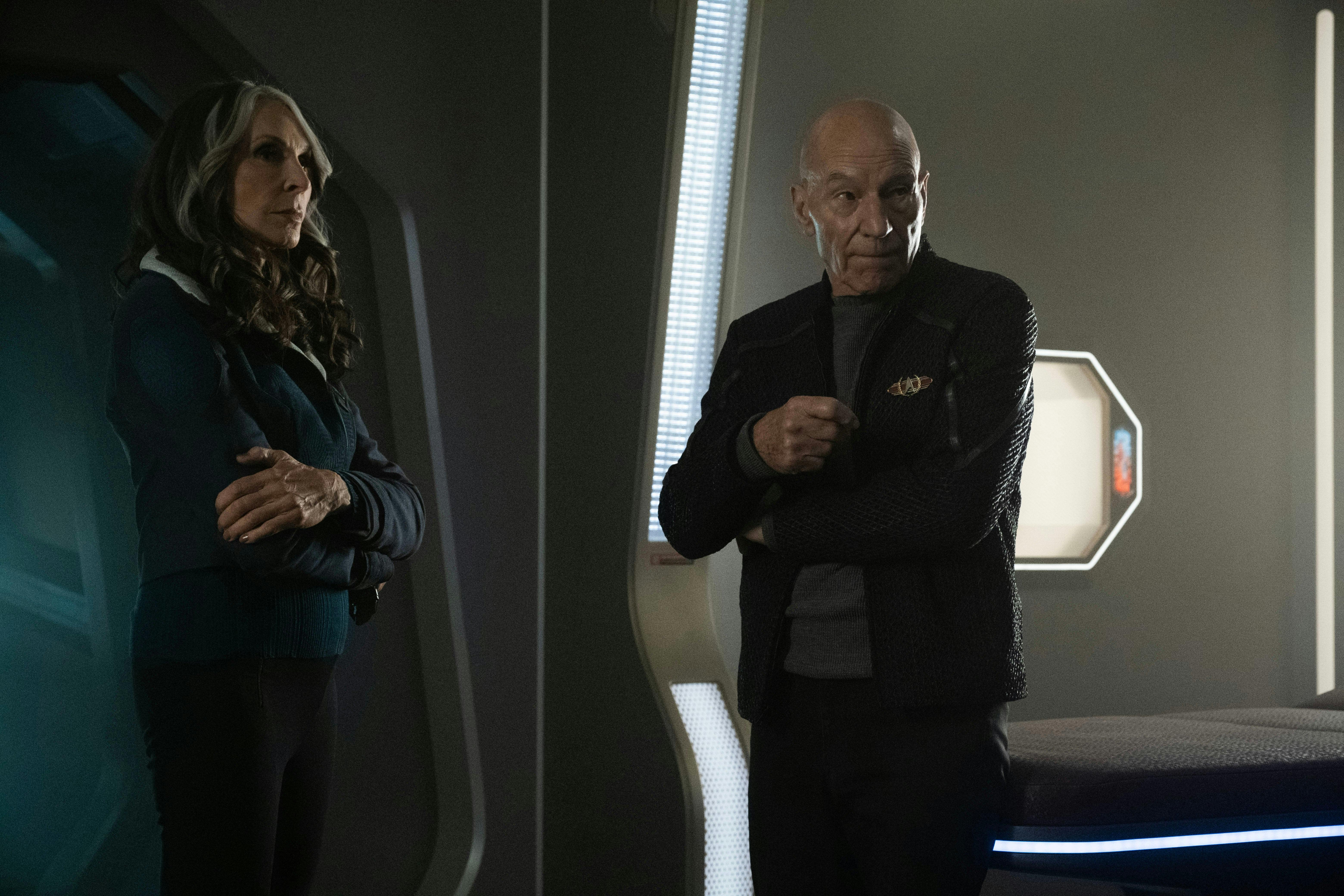 Dr. Beverly Crusher and Picard stand both with their arms crossed over themselves