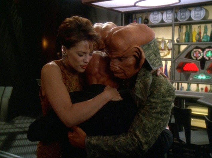 Leeta and Rom embrace Nog in a hug at Quark's Bar